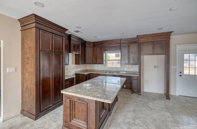 kitchen with dark brown cabinets, light stone countertops, a textured ceiling, and a kitchen island