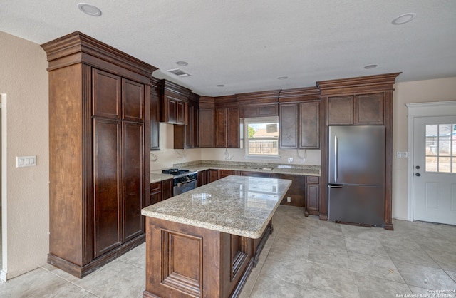 kitchen with light stone counters, stainless steel appliances, dark brown cabinets, and a center island