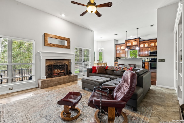 living room with a towering ceiling, a tiled fireplace, ceiling fan, and a wealth of natural light