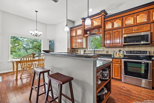 kitchen with dark hardwood / wood-style floors, backsplash, a kitchen bar, an inviting chandelier, and appliances with stainless steel finishes