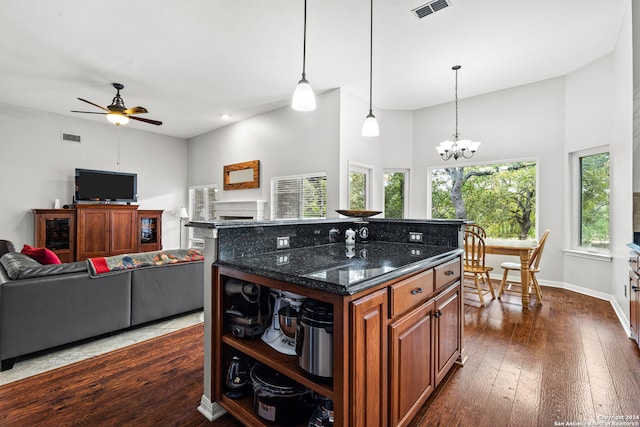 kitchen with a kitchen island, ceiling fan with notable chandelier, pendant lighting, dark wood-type flooring, and dark stone countertops