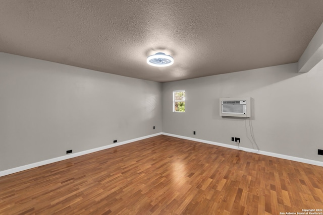 empty room featuring a textured ceiling, a wall mounted AC, and hardwood / wood-style flooring