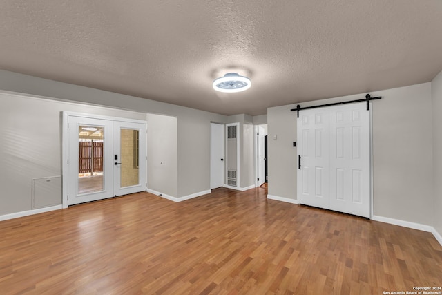 empty room with a textured ceiling, a barn door, wood-type flooring, and french doors