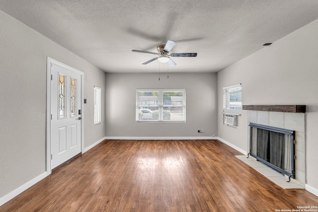 unfurnished living room with cooling unit, hardwood / wood-style floors, a textured ceiling, a fireplace, and ceiling fan