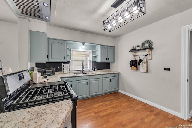 kitchen featuring a textured ceiling, light wood-type flooring, pendant lighting, stainless steel range with gas cooktop, and sink