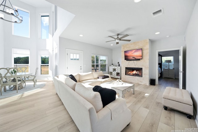 living room with light hardwood / wood-style flooring, a tiled fireplace, and ceiling fan with notable chandelier