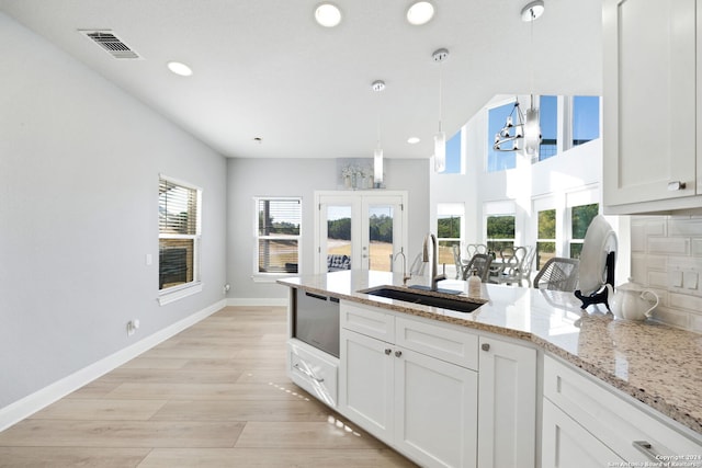 kitchen featuring tasteful backsplash, sink, white cabinetry, decorative light fixtures, and light hardwood / wood-style flooring