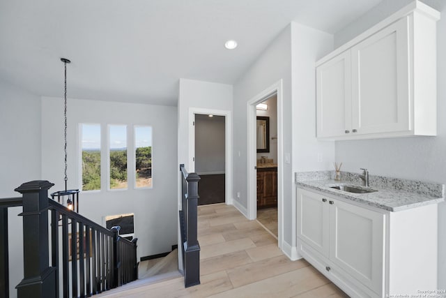 kitchen featuring light stone counters, white cabinetry, sink, and light wood-type flooring