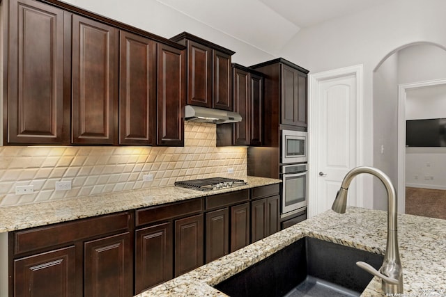 kitchen featuring backsplash, appliances with stainless steel finishes, vaulted ceiling, sink, and light stone counters