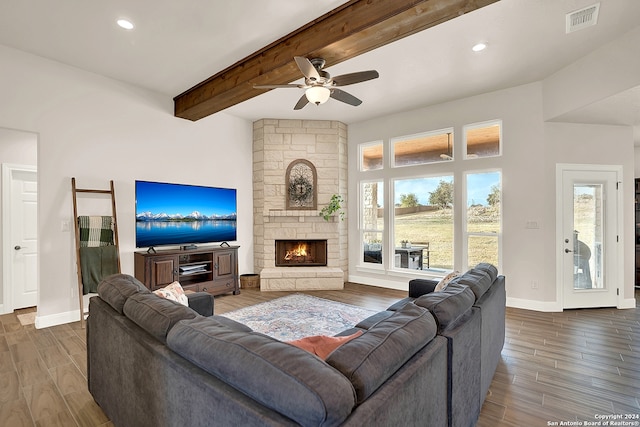 living room featuring beamed ceiling, a stone fireplace, dark hardwood / wood-style floors, and ceiling fan