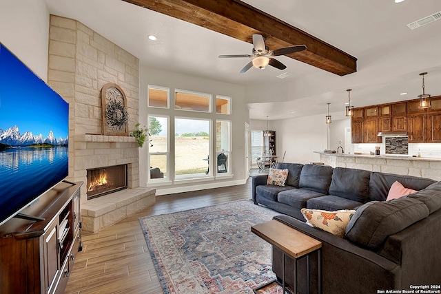 living room featuring ceiling fan, a stone fireplace, beamed ceiling, light hardwood / wood-style floors, and sink