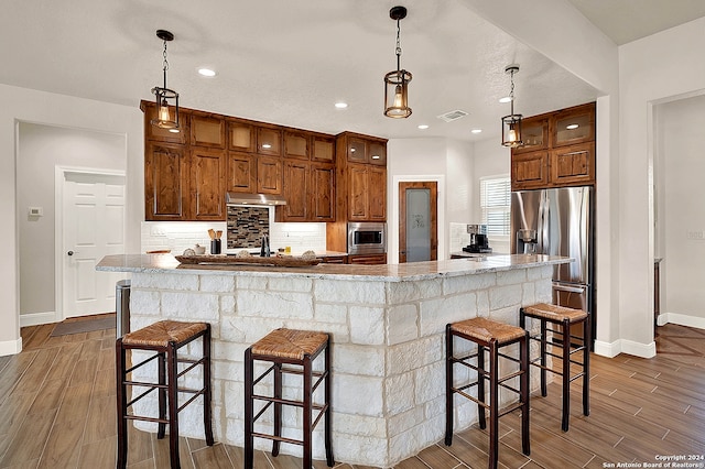 kitchen with appliances with stainless steel finishes, hardwood / wood-style floors, a kitchen island, and a breakfast bar area