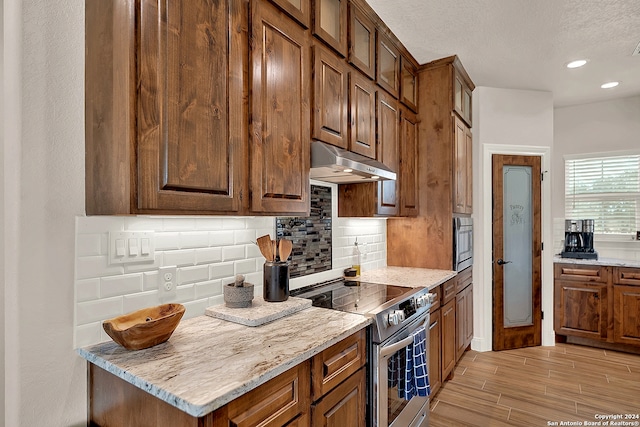 kitchen with stainless steel range with electric cooktop, backsplash, a textured ceiling, light hardwood / wood-style floors, and light stone counters