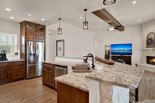 kitchen featuring sink, pendant lighting, light wood-type flooring, appliances with stainless steel finishes, and light stone counters