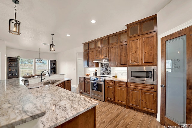 kitchen featuring sink, light stone countertops, decorative light fixtures, appliances with stainless steel finishes, and light hardwood / wood-style floors