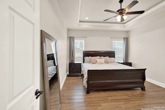 bedroom featuring light hardwood / wood-style floors, a raised ceiling, and ceiling fan