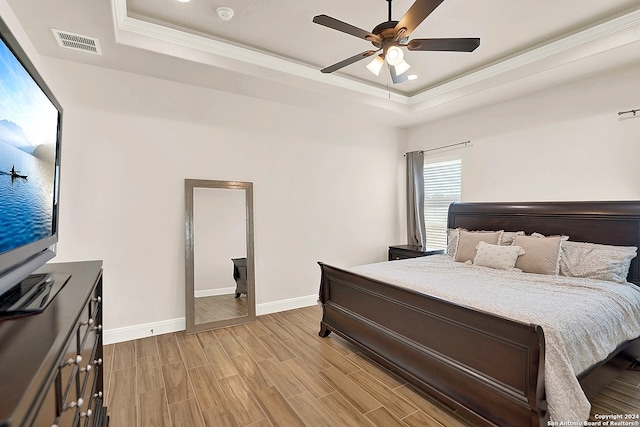 bedroom with ornamental molding, a tray ceiling, light wood-type flooring, and ceiling fan