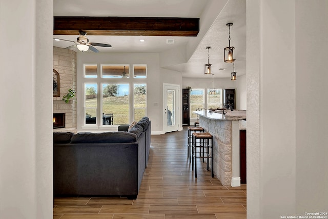 living room featuring beam ceiling, wood-type flooring, plenty of natural light, and ceiling fan