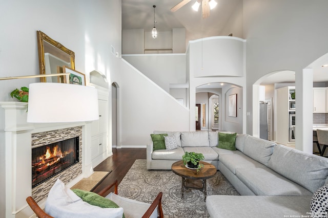 living room featuring dark wood-type flooring, a tile fireplace, a high ceiling, and ceiling fan