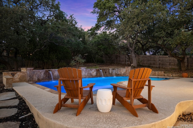 pool at dusk with a patio and pool water feature