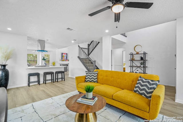 living room with light hardwood / wood-style floors, a textured ceiling, and ceiling fan