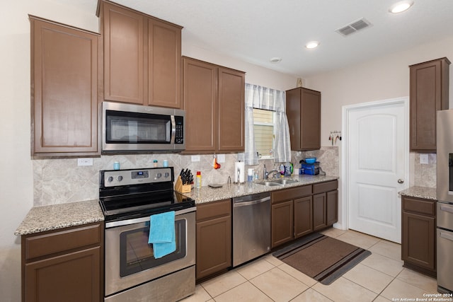 kitchen with decorative backsplash, light stone countertops, stainless steel appliances, and light tile patterned floors