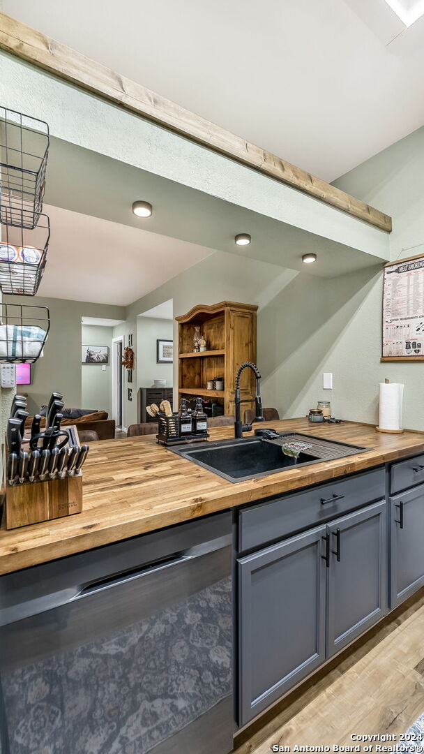 kitchen featuring sink, light hardwood / wood-style flooring, gray cabinets, wooden counters, and dishwasher