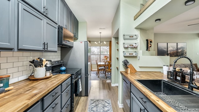 kitchen featuring butcher block counters, sink, tasteful backsplash, decorative light fixtures, and black appliances