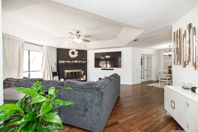 living room featuring a fireplace, dark hardwood / wood-style flooring, a tray ceiling, and ceiling fan with notable chandelier