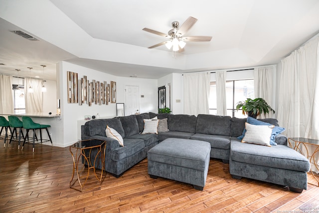 living room with a raised ceiling, ceiling fan, and hardwood / wood-style floors