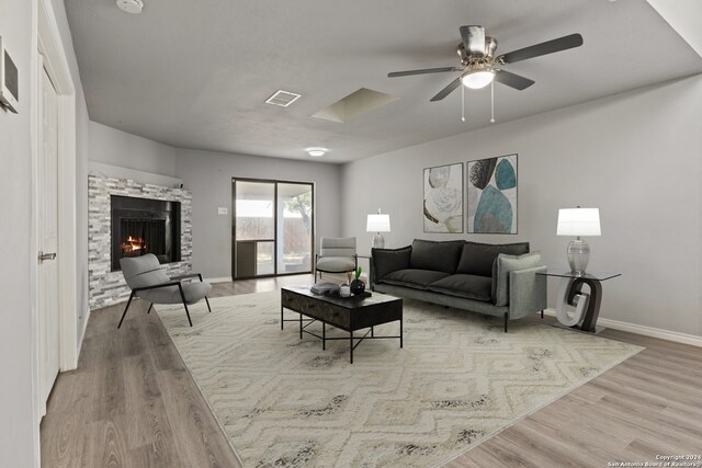 living room with a fireplace, light wood-type flooring, and ceiling fan