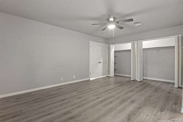 unfurnished bedroom with two closets, light wood-type flooring, and ceiling fan