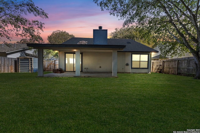 back house at dusk featuring a patio, a yard, and a shed