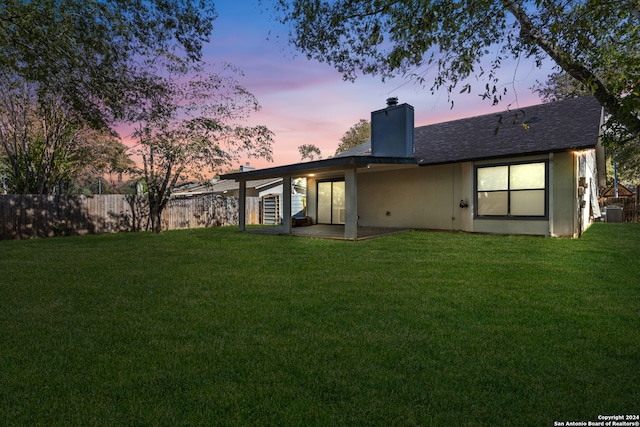 back house at dusk with a yard and central air condition unit