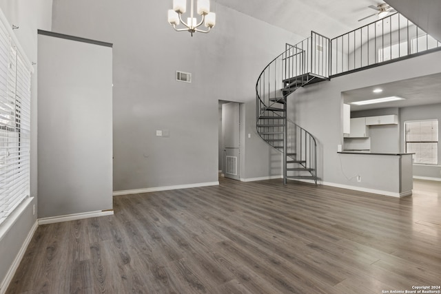 unfurnished living room with dark wood-type flooring, ceiling fan with notable chandelier, and a towering ceiling