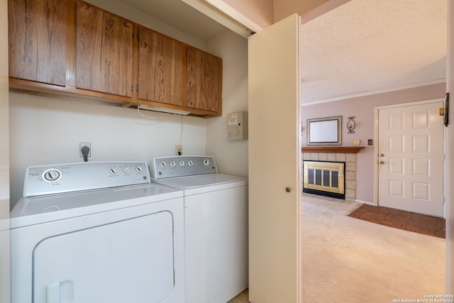 laundry area with light carpet, crown molding, washing machine and clothes dryer, cabinets, and a textured ceiling