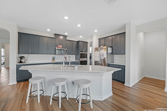 kitchen with backsplash, appliances with stainless steel finishes, light hardwood / wood-style flooring, and an island with sink