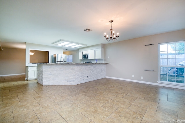 kitchen with kitchen peninsula, light stone countertops, white cabinetry, a chandelier, and appliances with stainless steel finishes