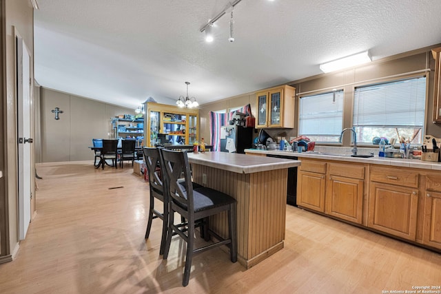 kitchen featuring sink, light wood-type flooring, a center island, decorative light fixtures, and a breakfast bar area