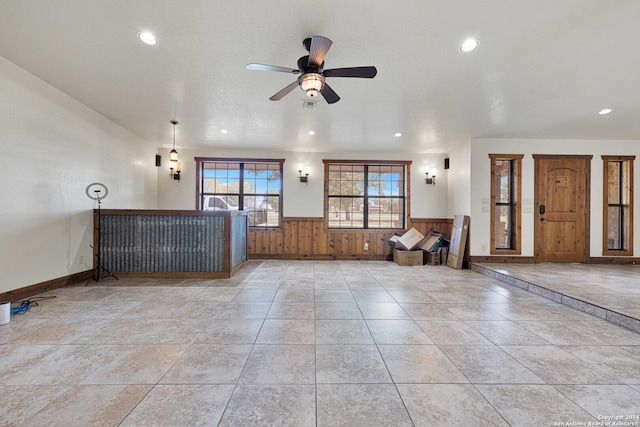 unfurnished living room with wooden walls, a textured ceiling, and ceiling fan