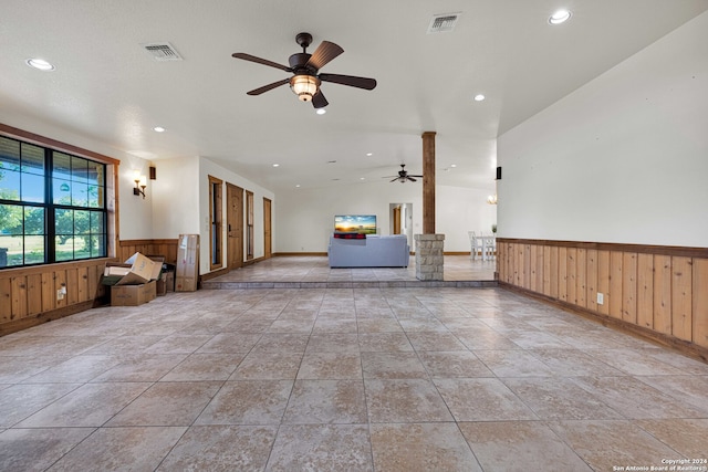 unfurnished living room with lofted ceiling, wood walls, and ceiling fan