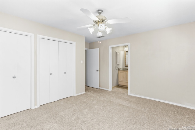 unfurnished bedroom featuring ensuite bath, multiple closets, light colored carpet, and ceiling fan