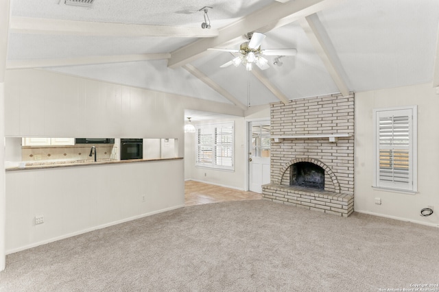 unfurnished living room featuring ceiling fan, a textured ceiling, a brick fireplace, vaulted ceiling with beams, and light colored carpet