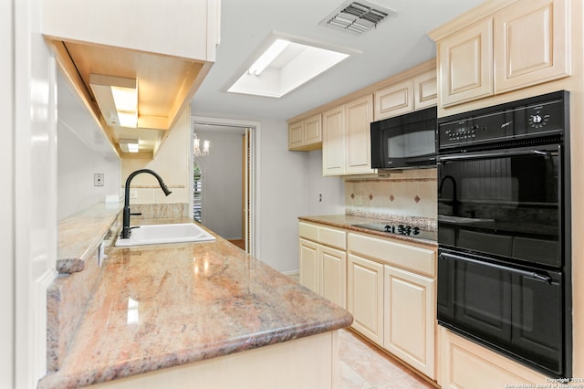 kitchen with light stone countertops, light tile patterned flooring, black appliances, cream cabinetry, and sink