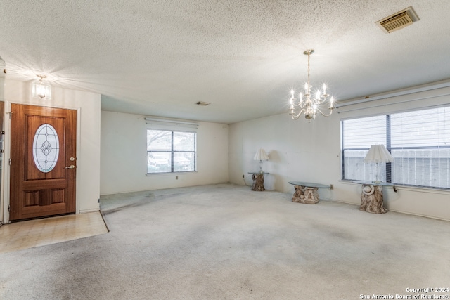 entrance foyer featuring light carpet, a notable chandelier, and a textured ceiling