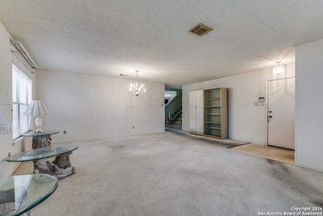 unfurnished living room with a textured ceiling, a chandelier, and light colored carpet