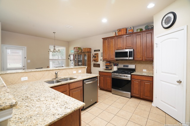 kitchen with sink, pendant lighting, an inviting chandelier, appliances with stainless steel finishes, and light stone counters