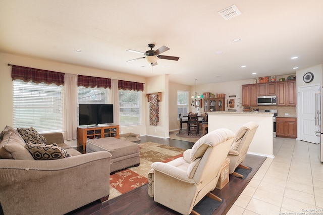 tiled living room with ceiling fan with notable chandelier