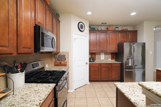 kitchen featuring light stone counters, appliances with stainless steel finishes, light tile patterned floors, and backsplash