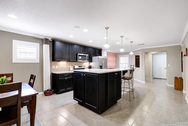 kitchen with a breakfast bar area, an island with sink, stainless steel appliances, ornamental molding, and decorative light fixtures